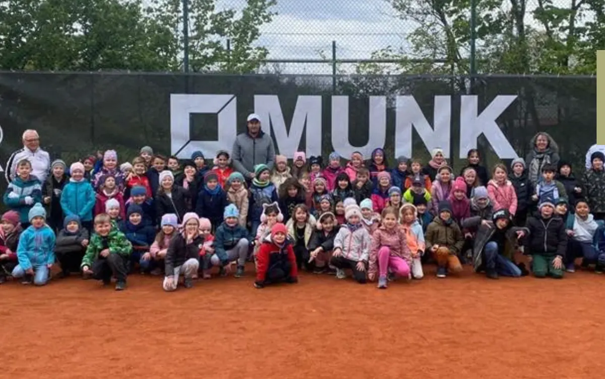 Große Kindergruppe beim Schnuppertennis auf dem Sandplatz vor dem Banner des Sponsors Munk